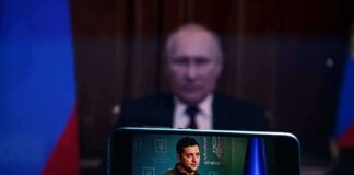 Vladimir Putin blurred in background behind smartphone showing a speech
