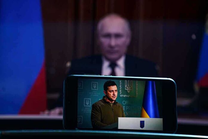 Vladimir Putin blurred in background behind smartphone showing a speech