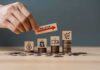Hand placing inflation label over stacked coins with economy icons