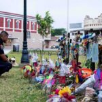 Police officer kneels at a memorial with flowers and crosses