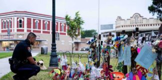Police officer kneels at a memorial with flowers and crosses