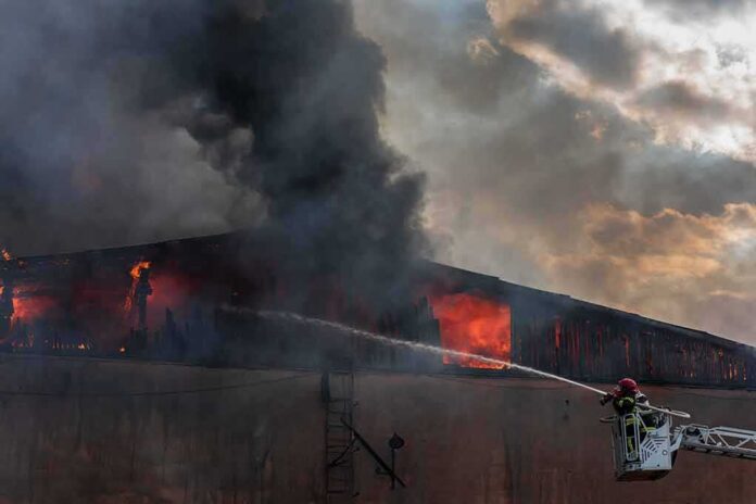 Firefighter on ladder spraying water at warehouse fire
