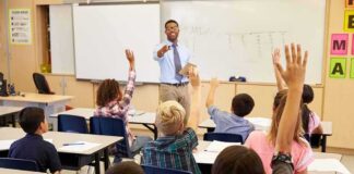 Teacher at front of classroom as students raise hands