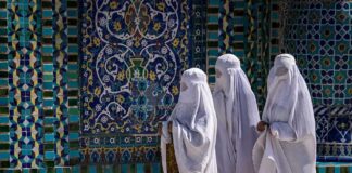 Three women in white veils walking past ornate blue tilework
