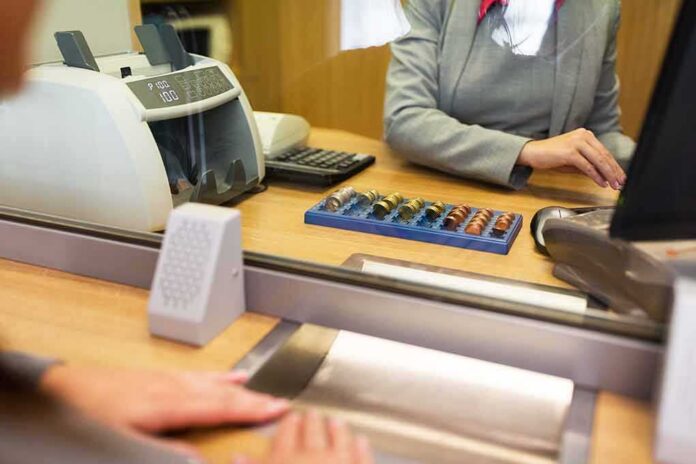 shutterstock_572920144 Bank teller at counter handling cash and coins