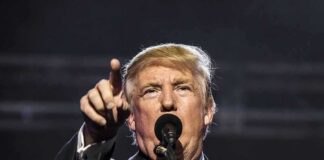 man speaking at a microphone and pointing forward