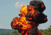 Fireball explosion with thick black smoke in open landscape
