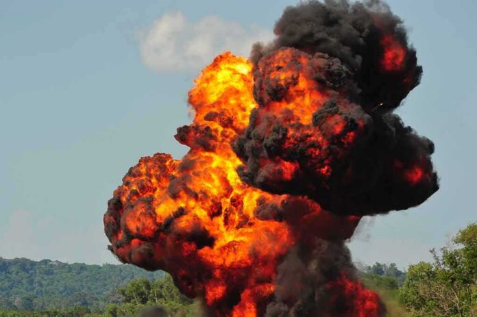 Fireball explosion with thick black smoke in open landscape