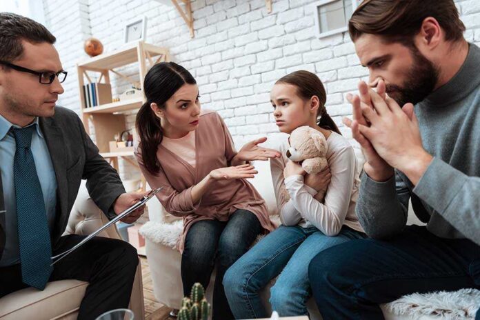 shutterstock_1054601264 Family and counselor in tense discussion with upset child holding teddy bear