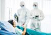 Medical staff in hazmat suits attend to a patient in a hospital bed