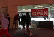 People outside a storefront with broken glass at night