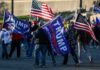 Crowd of people carrying political and American flags at a street gathering