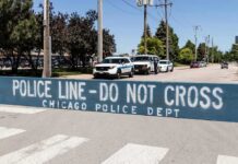 Police line barrier blocking a street with patrol vehicles behind