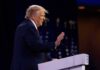 Donald Trump speaking at a podium with hand raised